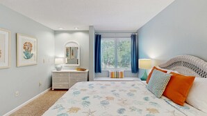 A bedroom with a bed, a dresser, a mirror, a window with curtains, and a lamp. - Beautiful home with natural light, lagoon views - Community Hot tub & Pool (Edisto Beach)