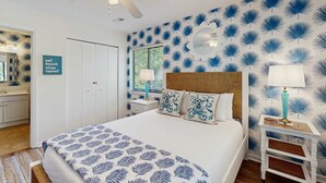 A bedroom with a bed, a ceiling fan, a nightstand, a mirror, and a wall with a leaf pattern. - Edisto condo with close proximity to beach & restaurants (Edisto Beach)