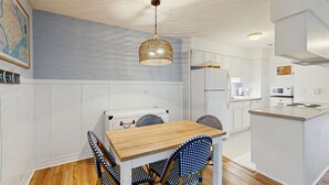 A modern kitchen with white cabinetry, a wooden dining table, blue patterned chairs, and a hanging pendant light. - Edisto condo with close proximity to beach & restaurants (Edisto Beach)