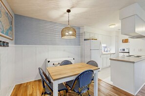 Eine moderne Küche mit weißen Schränken, einem Holzespeisetisch, blau gemusterten Stühlen und einer hängenden Pendelleuchte.
