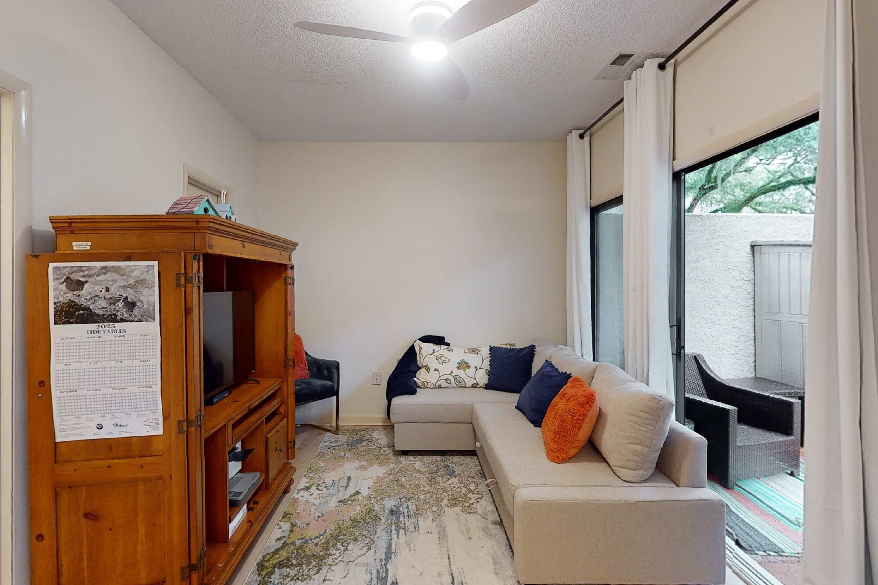 A living room with a sectional sofa, a wooden entertainment center, a ceiling fan, and a large window.