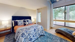 Ein Schlafzimmer mit einem großen Bett, einem Nachttisch, einer Bank, einem Fenster mit Blick auf Bäume und einem Deckenventilator.