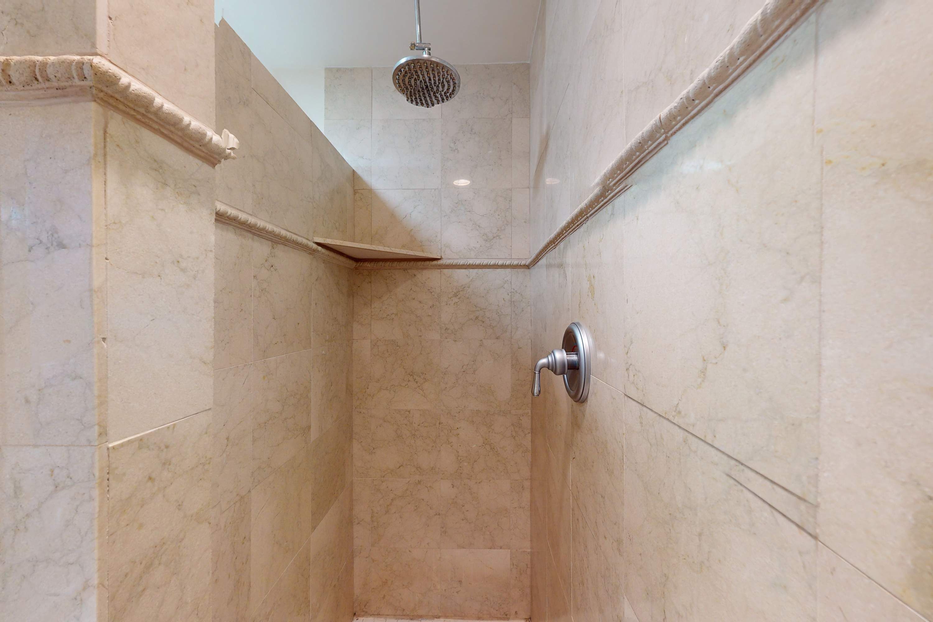 A corner shower with a handheld showerhead, marble walls, and a corner tile design.