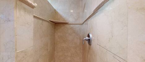 A corner shower with a handheld showerhead, marble walls, and a corner tile design.