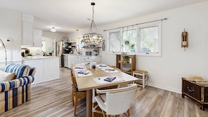 Una cucina moderna con mobili bianchi, una zona pranzo con tavolo e sedie in legno e un lampadario.