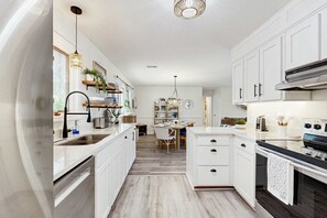 Une cuisine moderne avec des meubles blancs, des appareils en acier inoxydable et un coin repas comprenant une table et des chaises en bois.