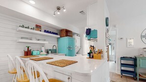 Een moderne keuken met witte kasten, een turquoise koelkast en een centraal eiland met stoelen.