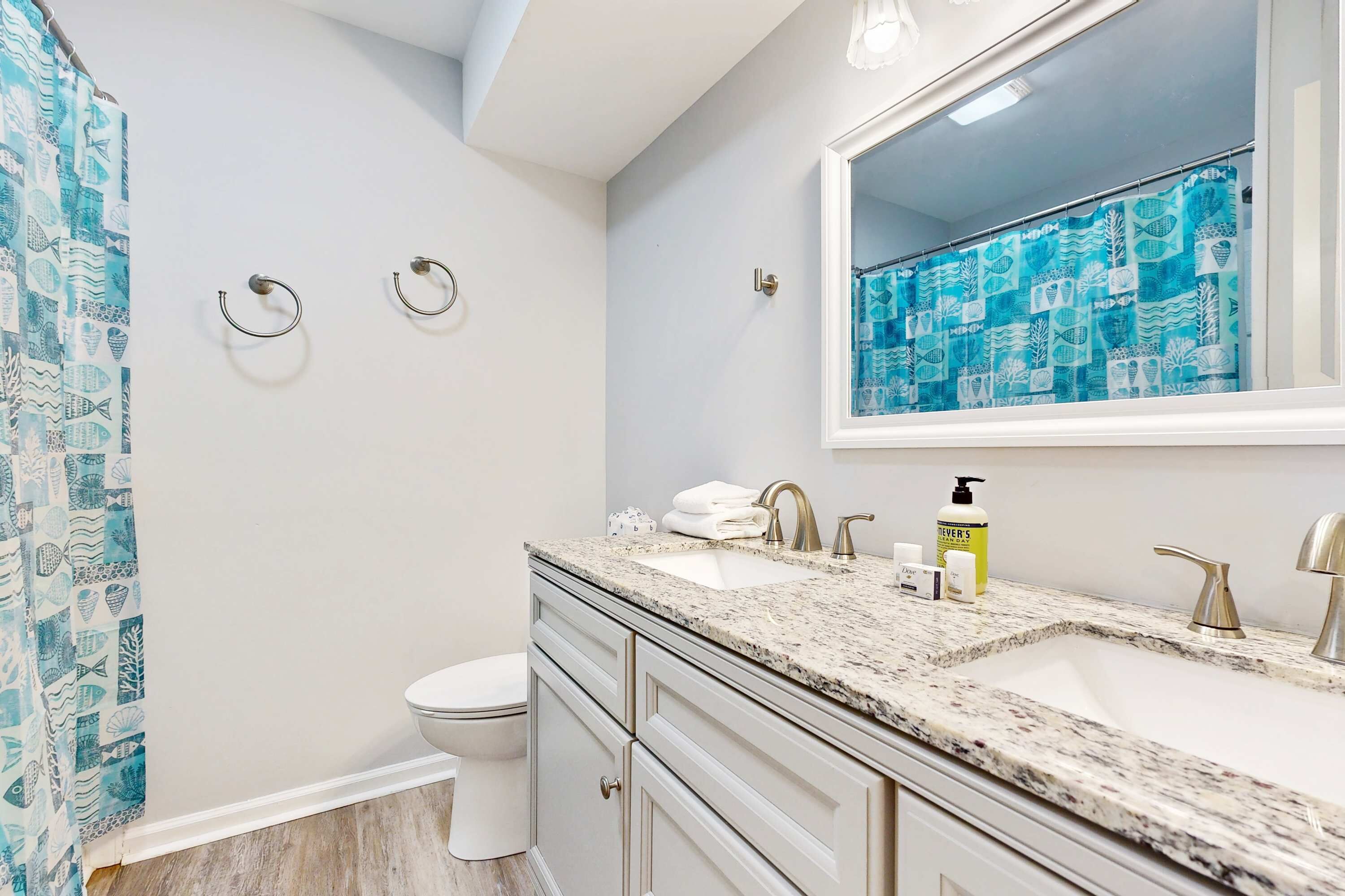 A bathroom with a white toilet, a sink with a marble countertop, and a shower curtain with a blue pattern.