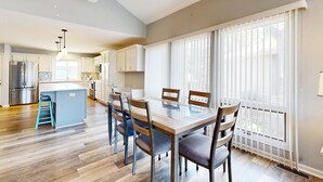 A modern kitchen with a central island, wooden chairs, and a dining table. - Coastal retreat with fireplace, AC, grill, lagoon views and close to beach (Edisto Beach)