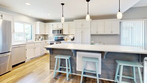 A modern kitchen with white cabinets, a large island with stools, and pendant lighting. - Coastal retreat with fireplace, AC, grill, lagoon views and close to beach (Edisto Beach)