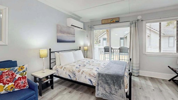 A bedroom with a bed, bedside tables, a chair, a window with curtains, and a view of the outside. - Charming & sun-filled studio with great patio & W/D - close to beach (Edisto Beach)