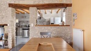 Eine rustikale Küche mit Steinwänden, Holzbalken, einem Edelstahlkühlschrank und einem Holzessttisch.