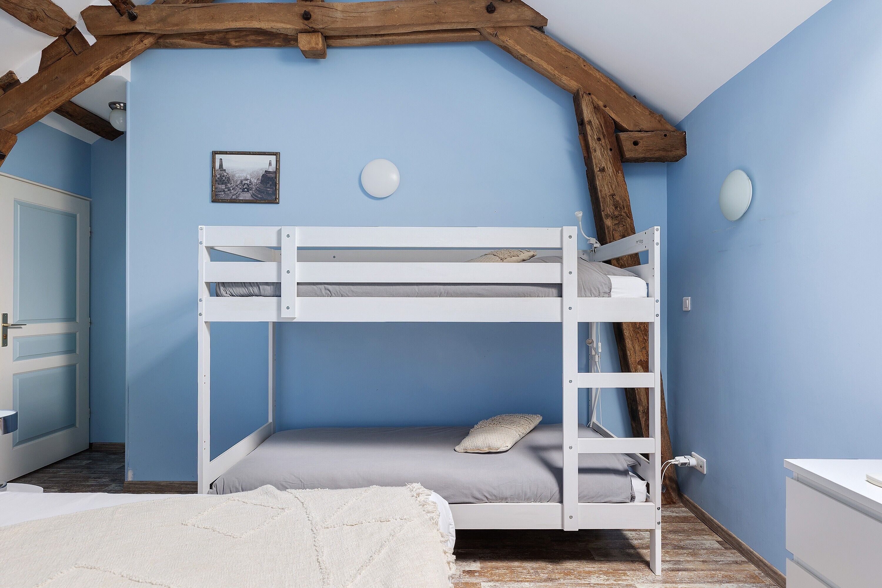 Quarto com beliche, teto de madeira, porta branca e mesinha de cabeceira.