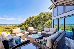 A balcony with wicker furniture and a glass table, overlooking a lush landscape and the sea. - Stunning Oceanfront Hideaway with Private Pool, Deck, and Yard - Dogs Welcome (Hilton Head)