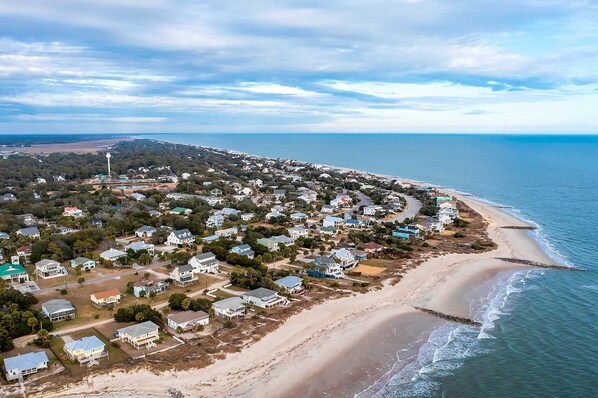 An aerial view of a coastal residential area with houses, a beach, and a lighthouse. - Custom home with private pool, elevator & short walk to the beach (Edisto Beach)