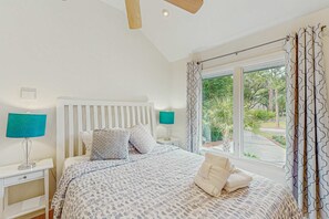 Ein Schlafzimmer mit einem Bett, zwei Nachttischen, einem Fenster mit Vorhängen und Blick ins Grüne.