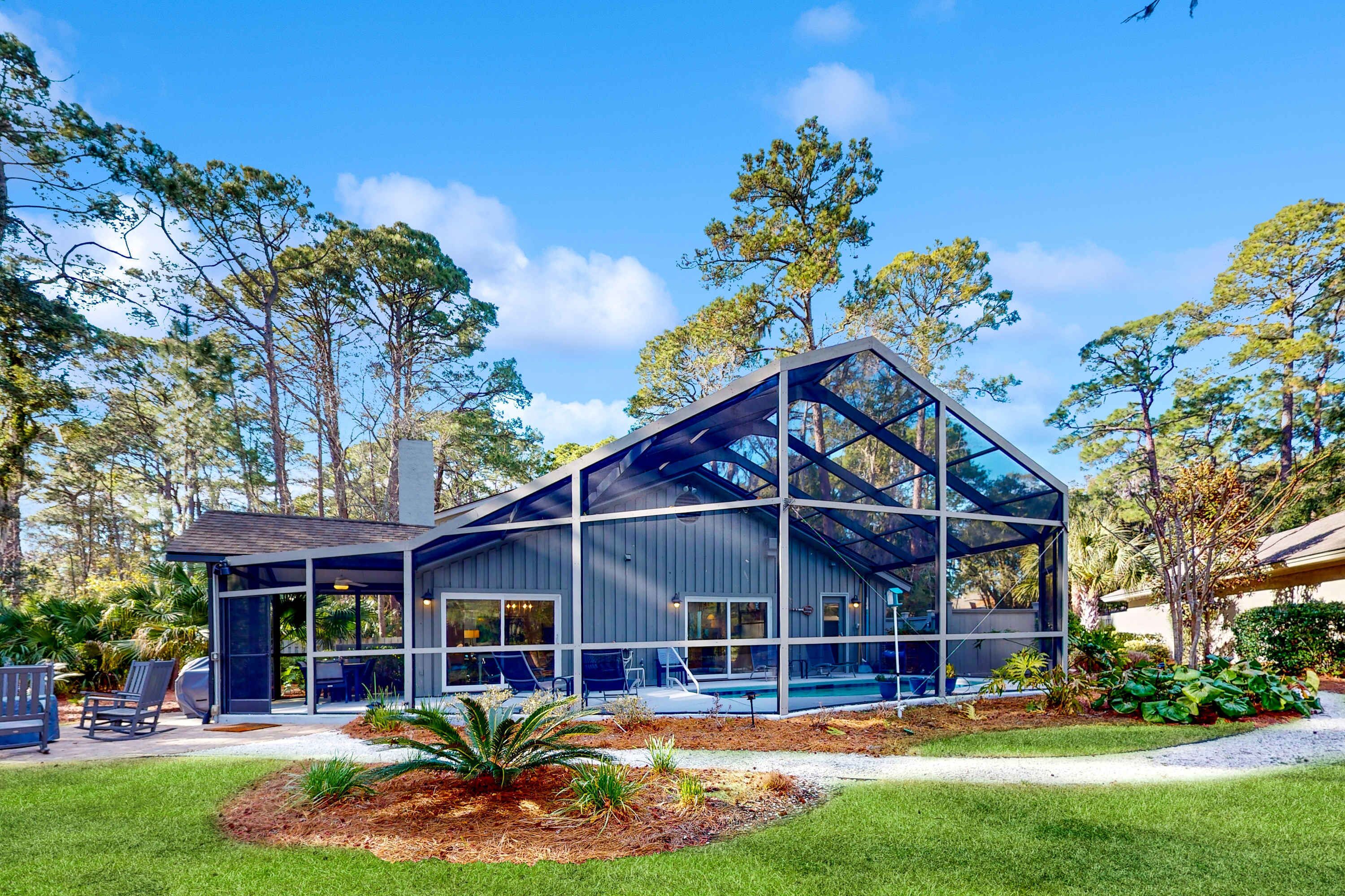 A modern house with a glass-enclosed patio, a swimming pool, and a well-maintained lawn.