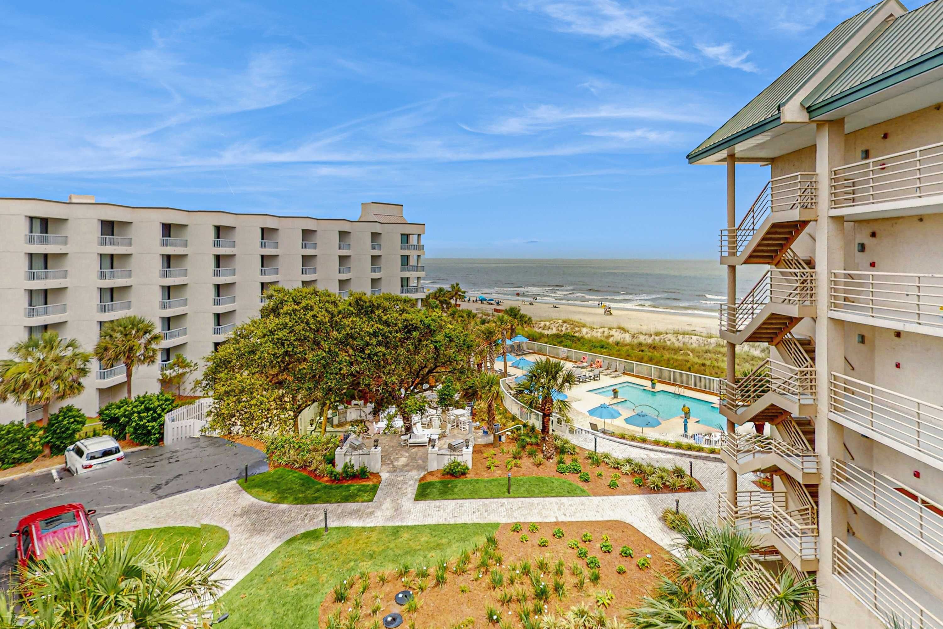 A hotel with a pool, a beach view, and a parking area.