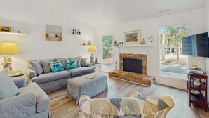 Una sala de estar con sofá, reposapiés y sillón, chimenea, televisión y obras de arte en las paredes.