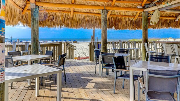 Restaurante frente al mar con terraza al aire libre, cubierta de madera y techo de paja.