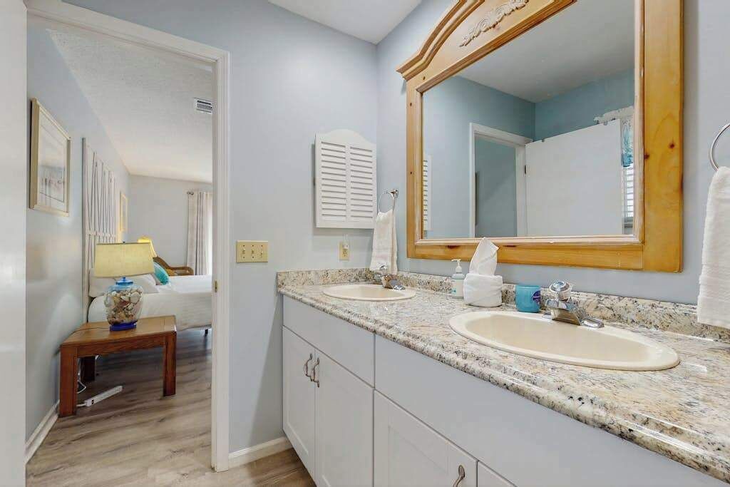 A bathroom with two sinks, a large mirror, and a small table with a lamp.