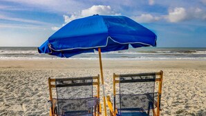 Escena de playa con una sombrilla azul, dos sillas de playa y el océano al fondo.