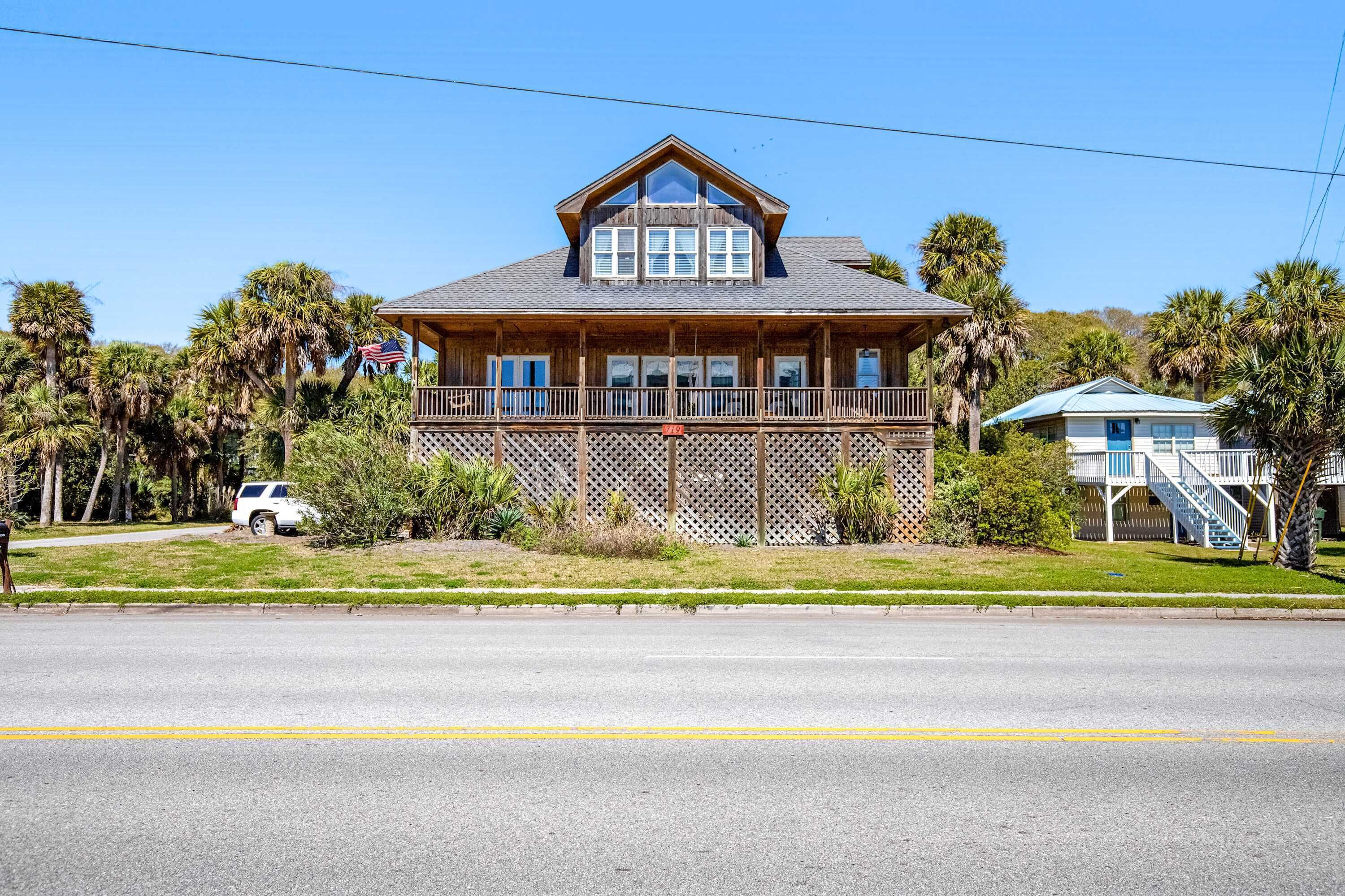 A two-story wooden house with a balcony, surrounded by palm trees.
