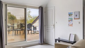 Une pièce dotée d’une porte-fenêtre coulissante donnant sur une terrasse extérieure, d’un lit, d’une petite table et d’un mur orné d’affiches informatives.