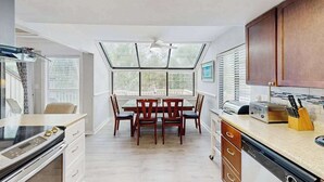 A modern kitchen with a dining table, wooden cabinets, and a large window. - Sunny Villa with Spacious Decks, Al Fresco Dining, & Shared Pool - Nearby Beach Access (Hilton Head)