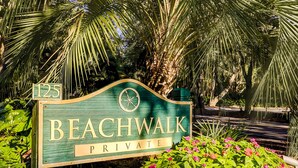 A sign for 'Beachwalk Private' with a compass symbol, surrounded by lush greenery and flowering plants. - Sunny Villa with Spacious Decks, Al Fresco Dining, & Shared Pool - Nearby Beach Access (Hilton Head)