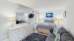 A bedroom with a bed, a dresser, a television, and a nightstand with lamps. - Sunny Villa with Spacious Decks, Al Fresco Dining, & Shared Pool - Nearby Beach Access (Hilton Head)