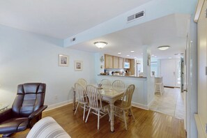 A dining area with a glass-top table and white chairs, a leather chair, and wooden flooring. - Sunlit Sea Escape with Al Fresco Dining, Loft, Grill, Shared Pool (Hilton Head)