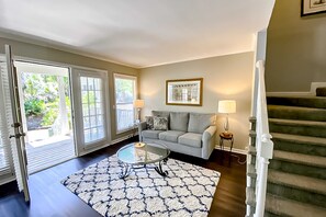 A living room with a sofa, a coffee table, a lamp, and a staircase. - Water view condo with covered deck, on site golf, AC, & WD close to beach (Hilton Head)