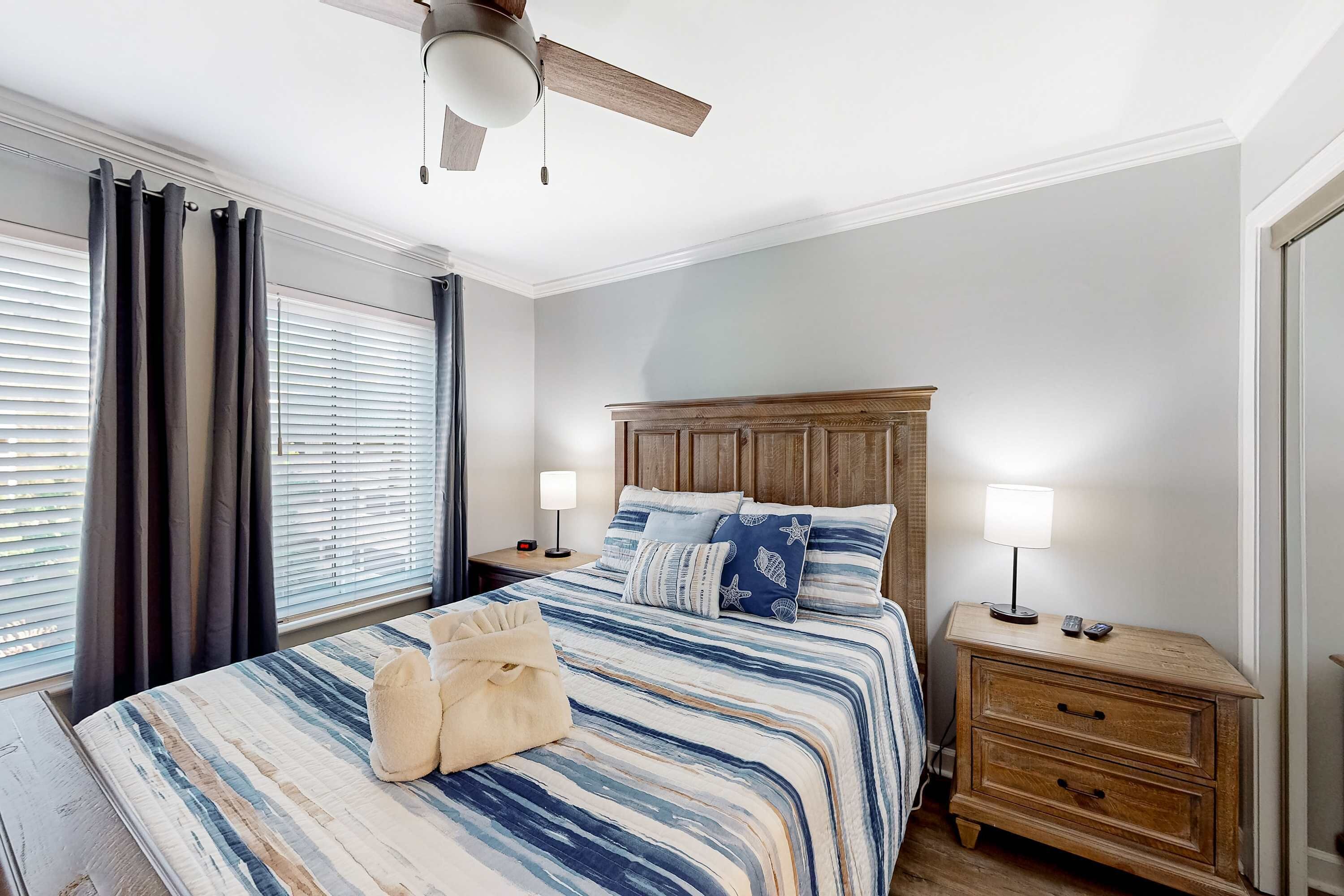 A bedroom with a bed, nightstands, a ceiling fan, and a window with curtains.
