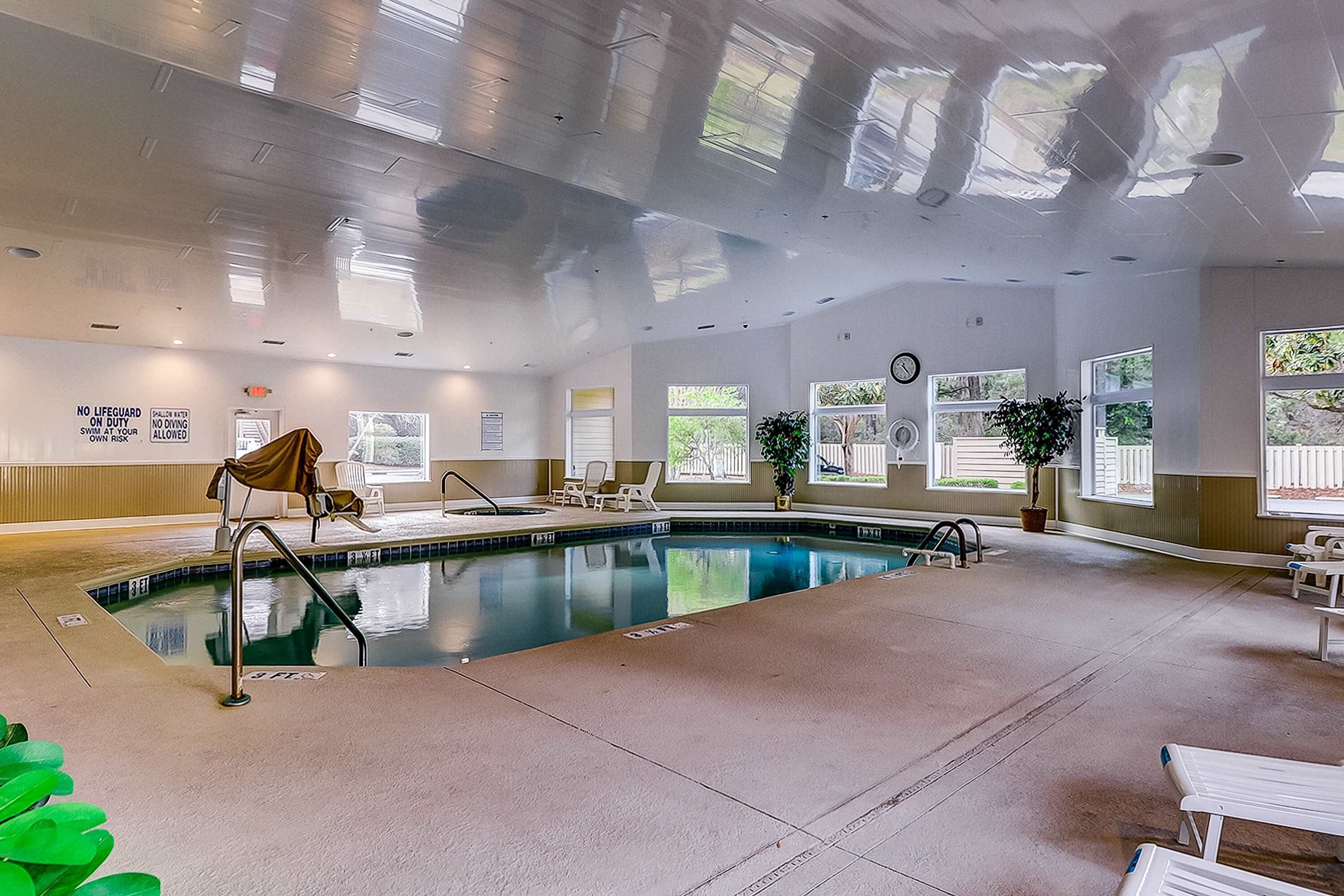 An indoor swimming pool with clear water, surrounded by lounge chairs and potted plants.