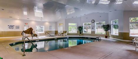 An indoor swimming pool with clear water, surrounded by lounge chairs and potted plants.
