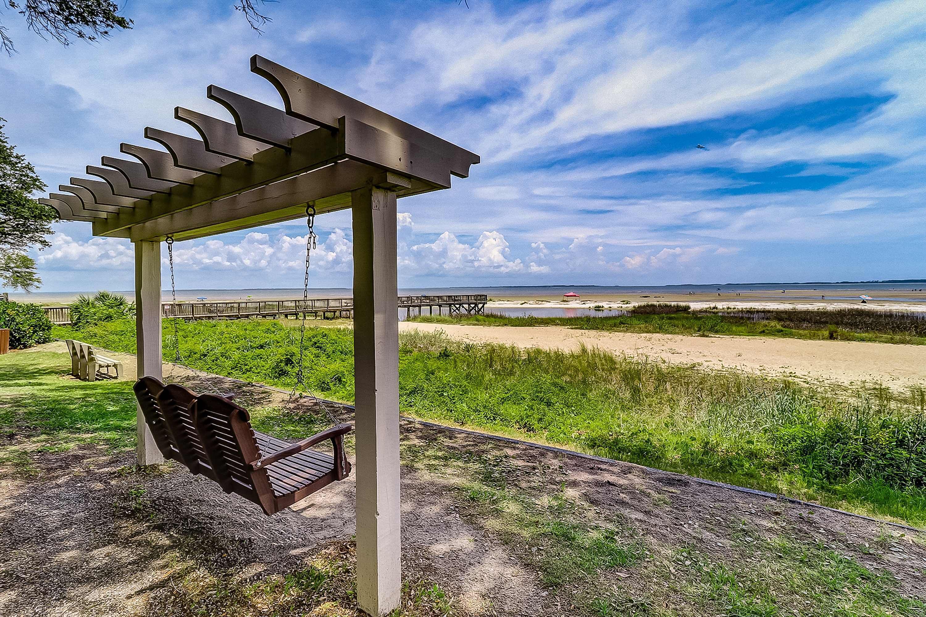 A wooden pergola with a swing, a bench, and a view of a beach and pier.