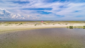 Ett kustlandskap med en sandstrand, en liten vattenyta och en röd byggnad i fjärran.