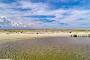 Un paisaje costero con una playa arenosa, una masa de agua pequeña y una estructura roja a lo lejos.