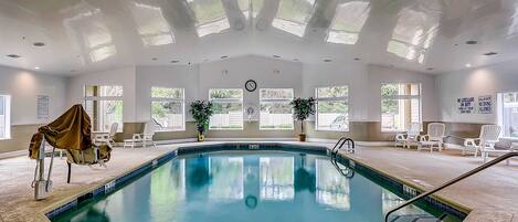 Una piscina interior con agua cristalina, rodeada de sillones de descanso y plantas en macetas.
