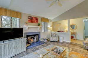 A living room with a fireplace, television, and a ceiling fan. - Welcoming Condo with Lagoon Views, Deck, Shared Pool & Nearby Beach Access (Hilton Head)