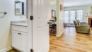 A room with a wooden floor, white cabinets, a dining area with a table and chairs, and a sofa.