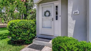 A white house with a door, a number 241 sign, and a wreath on the door.