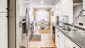 A modern kitchen with stainless steel appliances, white cabinetry, and a granite countertop.