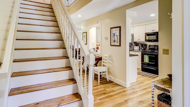 A staircase with wooden steps and white railings, leading to a dining area with a table and chairs.