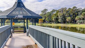 A wooden deck with a gazebo, a sign warning against feeding alligators, and a pond in the background.