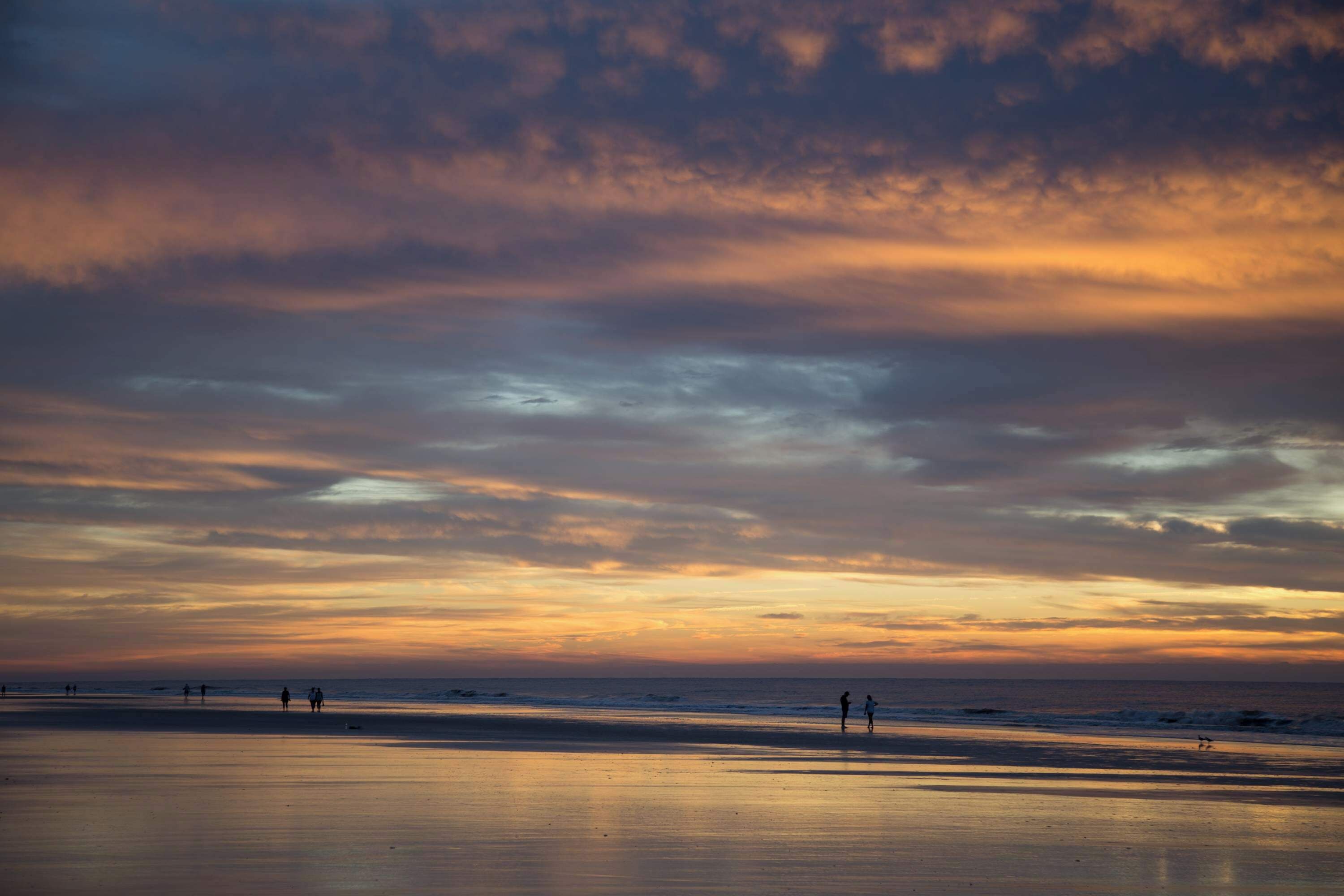 A beach with a sunset sky, calm sea, and distant figures.