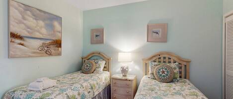 Una habitación con dos camas, una mesita de noche con lámpara, un cuadro en la pared y una ventana con persianas.
