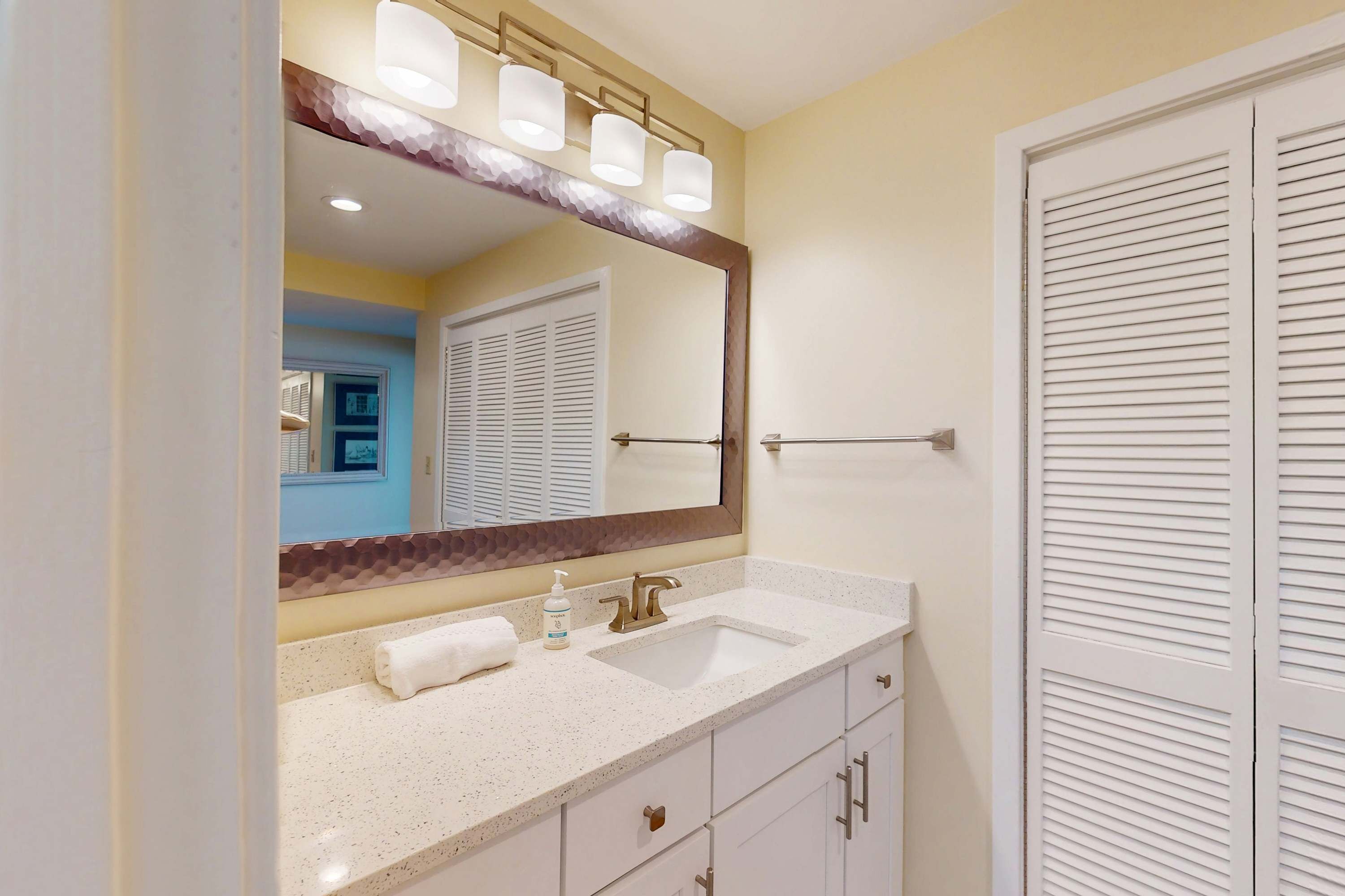 A bathroom with a large mirror, a sink, a towel, and a door with louvered panels.