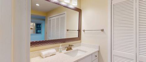 A bathroom with a large mirror, a sink, a towel, and a door with louvered panels.